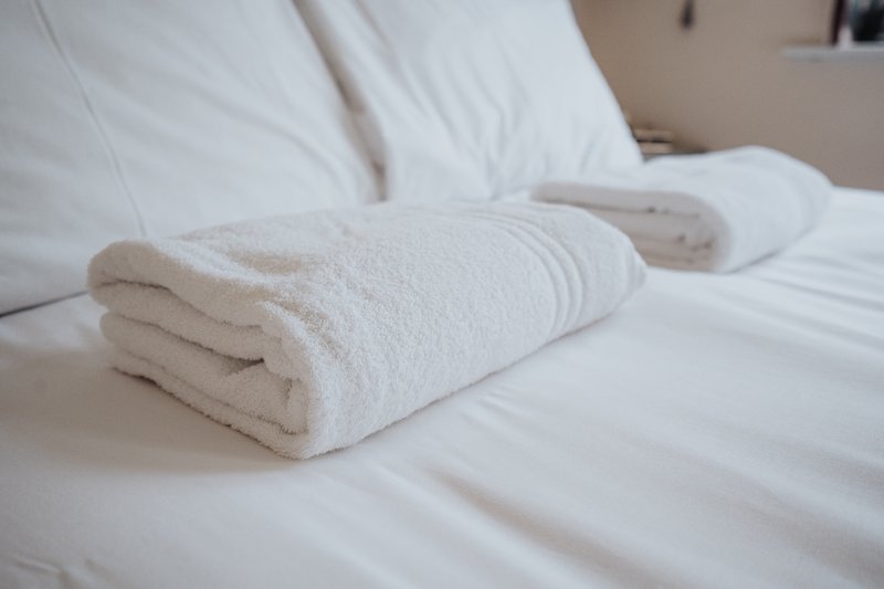 White rolled towels arranged on a made bed with pillows in background