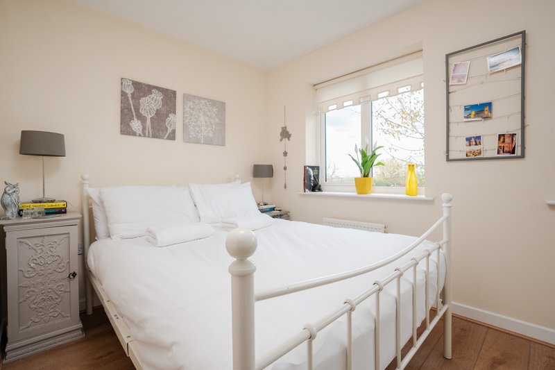 Bright bedroom with white metal bed frame, white bedding, wooden floor and window view