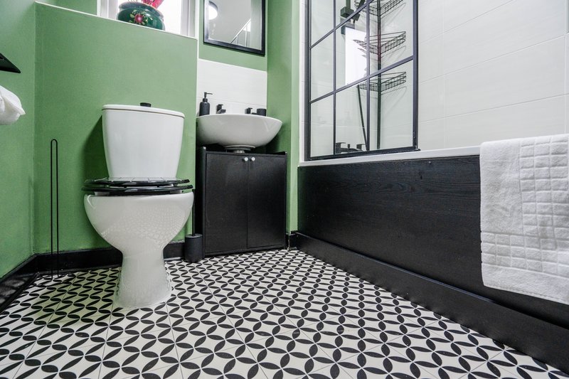 Modern bathroom with green walls, white toilet, black vanity, geometric floor tiles and white subway tile wainscoting