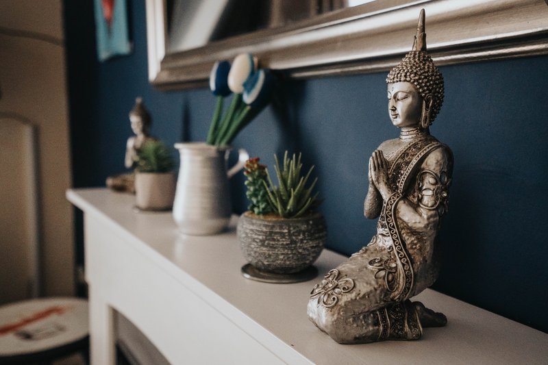 Bedroom shelf with decorative Buddha statue, potted plants and ceramic pitcher against blue wall