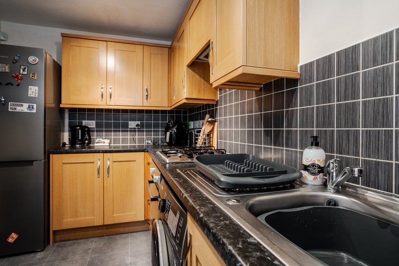 Kitchen with wooden cabinets, black tile backsplash, gas cooker and stainless steel sink
