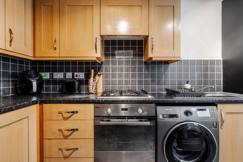 Modern kitchen with wooden cabinets, black tile backsplash, gas hob, oven and washing machine
