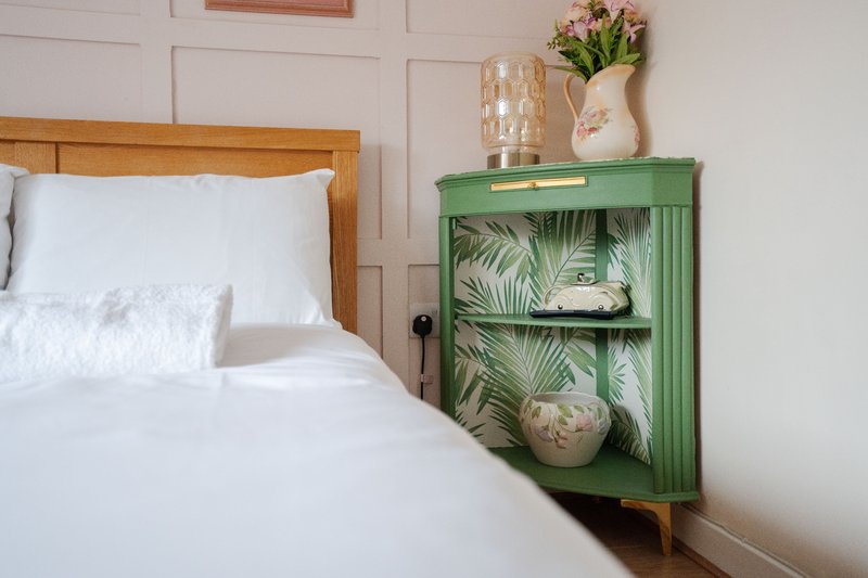 Bedroom with wooden bed frame, white bedding, and green corner cabinet with decorative items