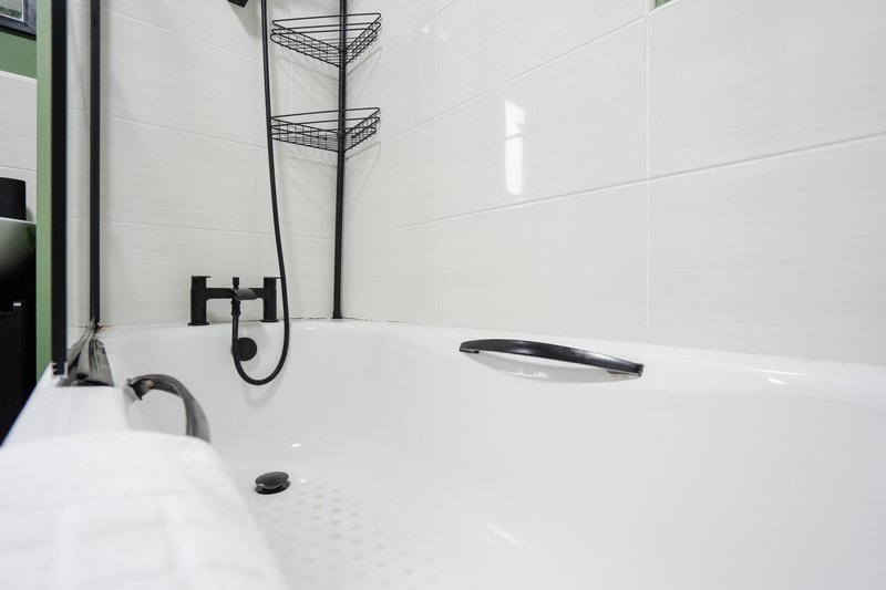 Modern white bathroom with bathtub, black fixtures, and wall-mounted shelving