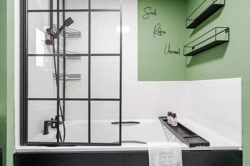 Modern bathroom with walk-in shower, green accent wall, shelving and white subway tile