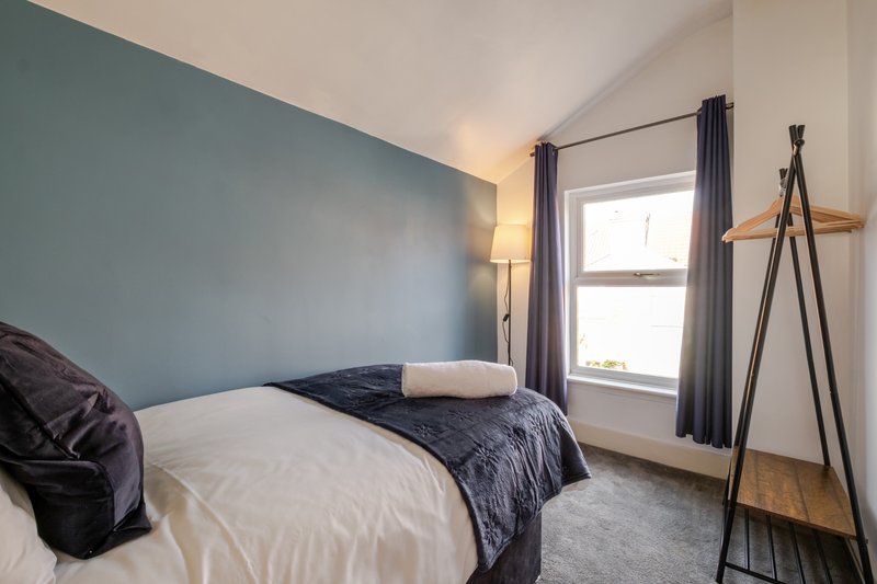 Bedroom with double bed, teal accent wall, window with gray curtains, and wooden coat stand