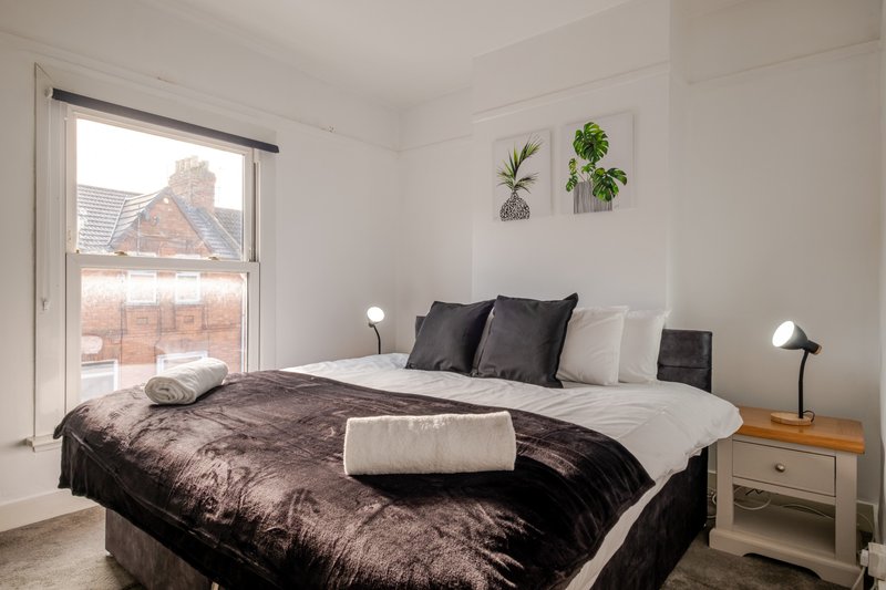 Bright bedroom with double bed, black bedding, potted plants on wall, and view of brick exterior