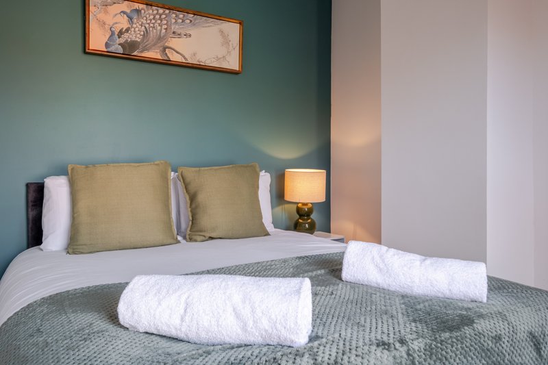 Modern bedroom with double bed, olive cushions, white towels and bedside lamp