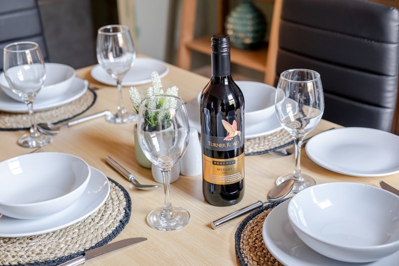 Formal dining table set with wine bottle, glasses, white plates and woven placemats