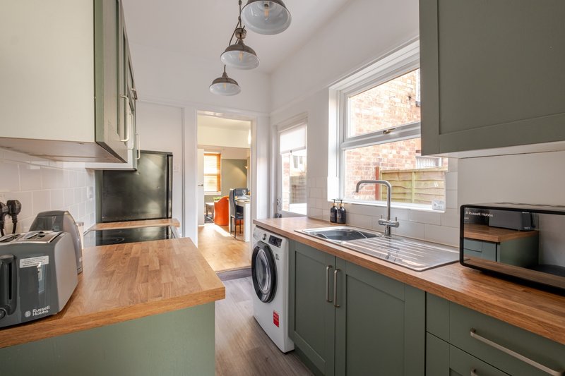 Modern kitchen with green cabinetry, wooden worktops, stainless steel appliances and pendant lights
