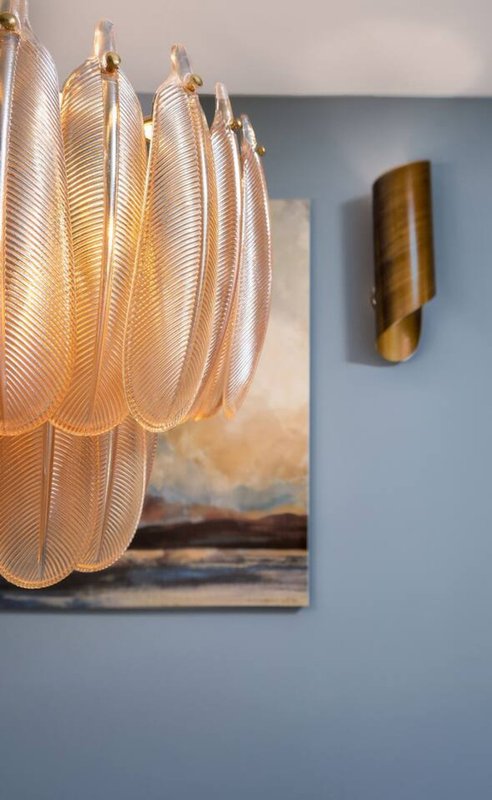 Blue wall with pendant lamp, framed landscape artwork, and brass wall sconce