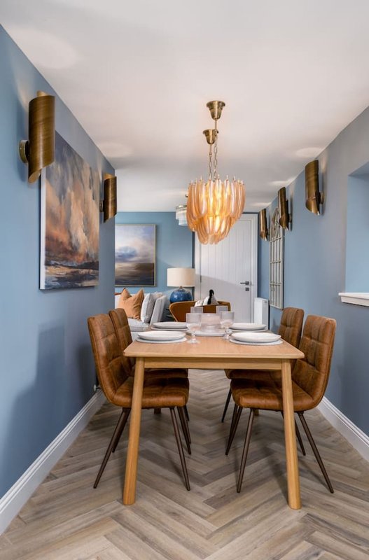 Modern dining room with wooden table, upholstered chairs, pendant light and blue walls