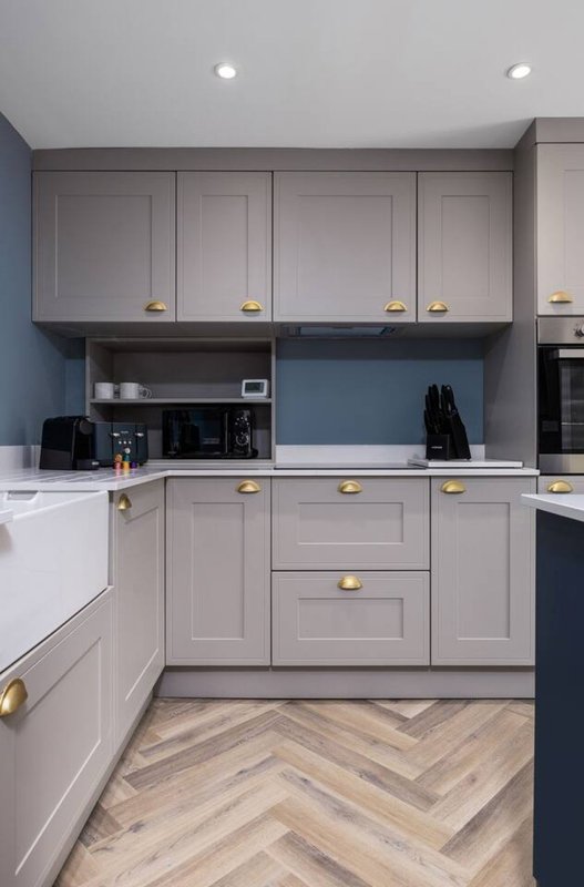 Modern kitchen with grey cabinetry, brass handles, blue accent wall, and herringbone flooring