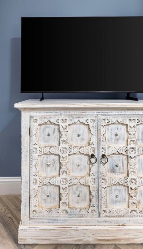 Flat-screen TV on whitewashed wooden cabinet with ornate carved doors