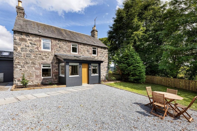 Stone cottage with gravel driveway, garden seating, and mature trees