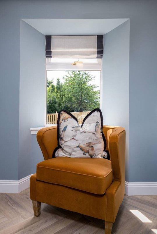 Tan leather armchair with patterned cushion facing window with garden view