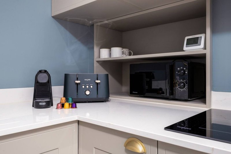 Modern kitchen with white countertop, open shelving, coffee machine, microwave and induction hob