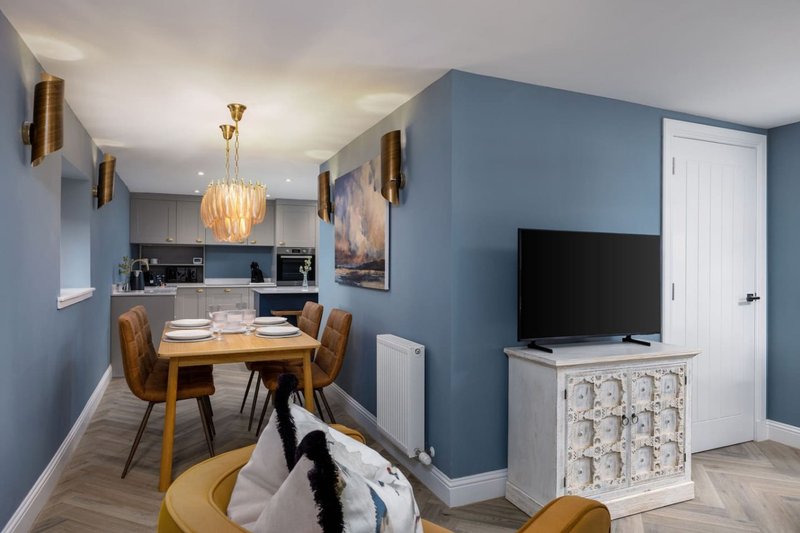 Modern open-plan living space with dining table, kitchen area, TV, and blue-painted walls