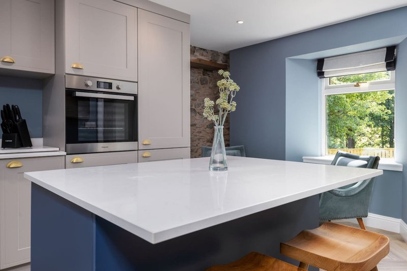 Modern kitchen with white countertop island, blue cabinetry, built-in oven and window seating