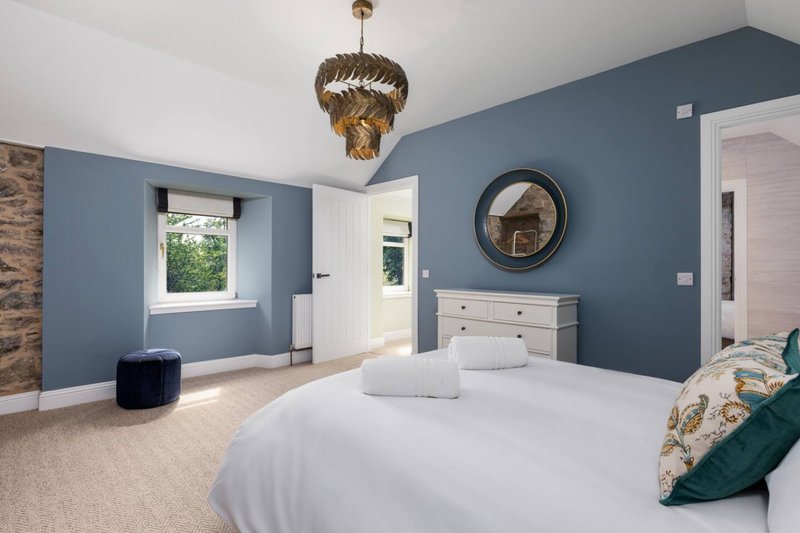 Spacious bedroom with blue walls, white bed, pendant light and round mirror