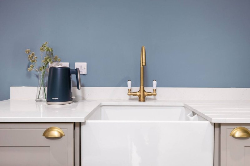Modern kitchen sink with white farmhouse basin, brass faucet, and blue-grey tiled backsplash