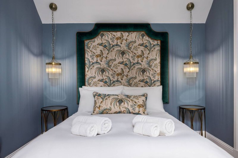 Modern bedroom with double bed, patterned headboard, white bedding, rolled towels, pendant lights, and blue walls