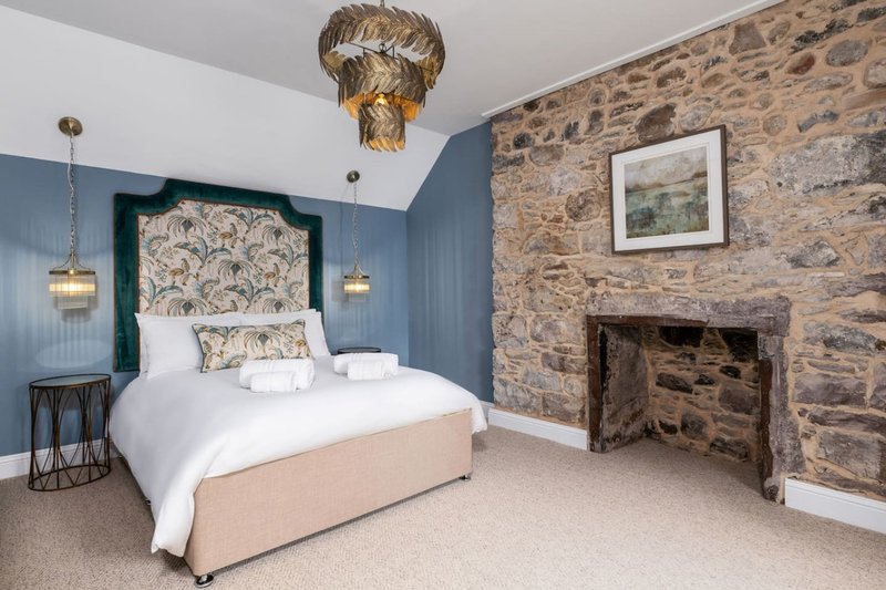 Bedroom with double bed, blue walls, stone fireplace, and gold ceiling fixture