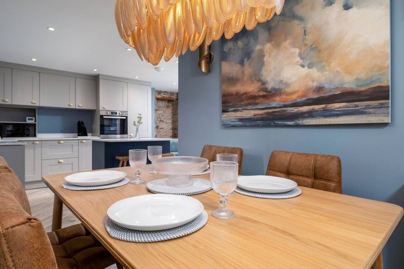 Open-plan dining and kitchen area with wooden table, place settings, pendant light and landscape artwork