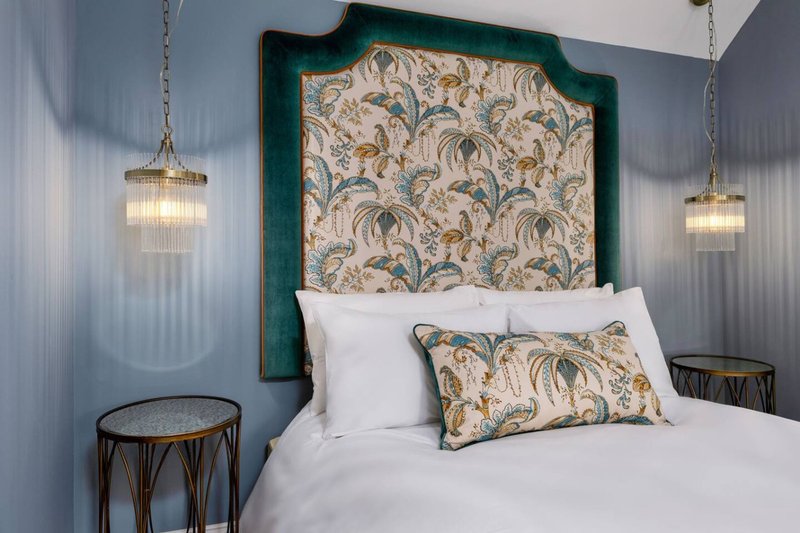 Bedroom with green upholstered headboard, white bedding, patterned pillow, and hanging pendant lights