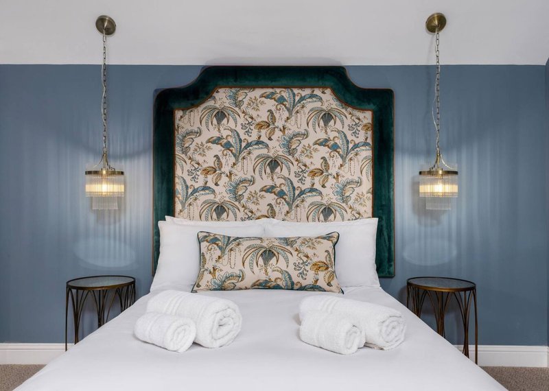 Modern bedroom with green upholstered headboard, white bedding, pendant lights, and patterned cushion