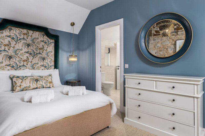 Bedroom with blue walls, double bed, white dresser, round mirror and en-suite bathroom visible
