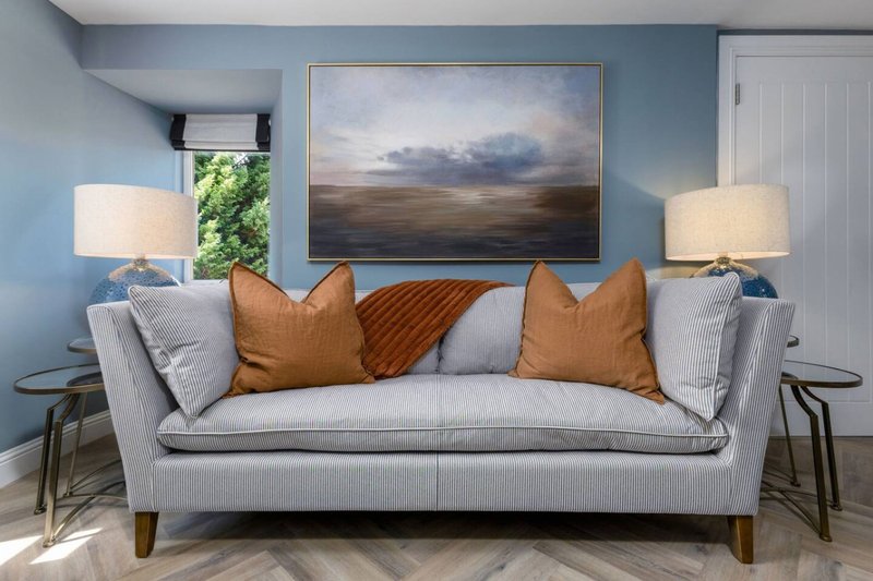 Modern living room with gray sofa, orange cushions, landscape artwork and table lamps