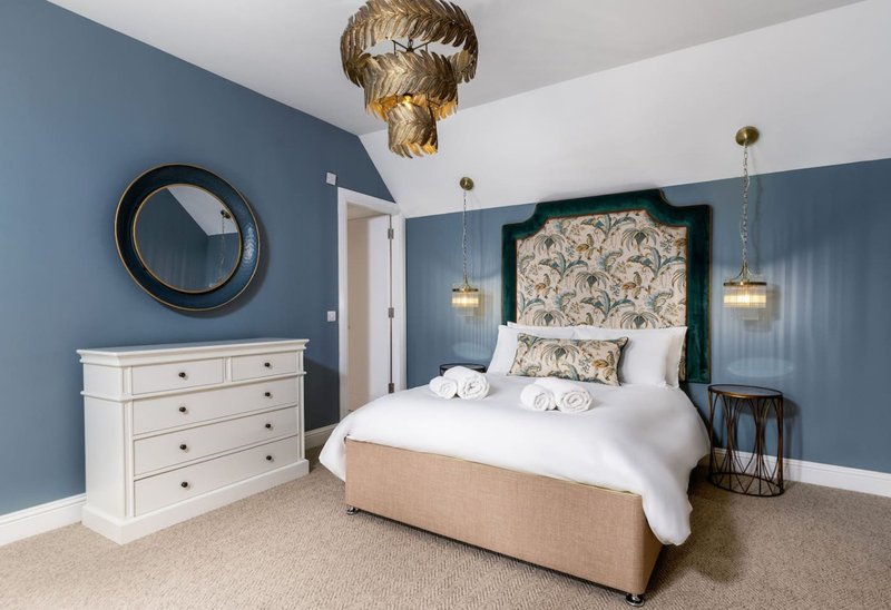 Bedroom with blue walls, white furniture, patterned headboard and gold ceiling fixture