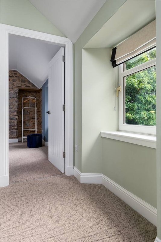 Light hallway with open doorway, window with blinds, and cream carpet flooring