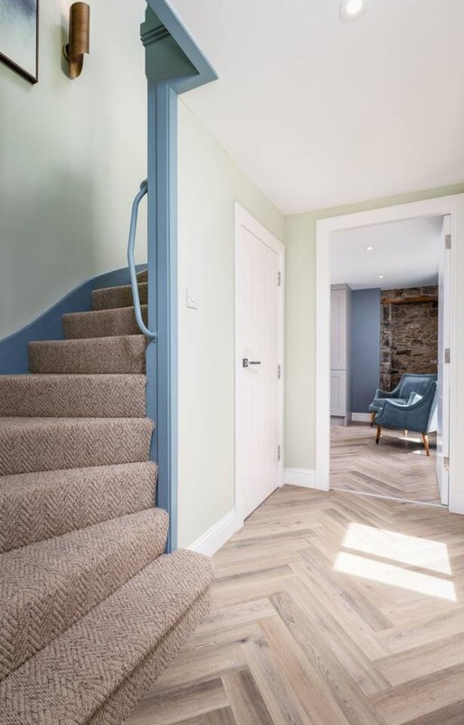 Bright hallway with blue-painted staircase, herringbone wood flooring, white doors and walls