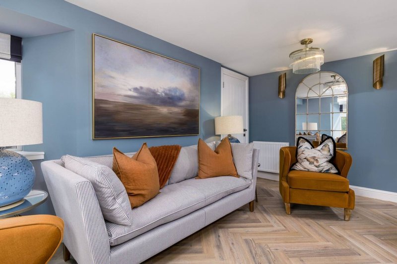 Modern living room with blue walls, grey sofa, orange cushions and wooden armchair