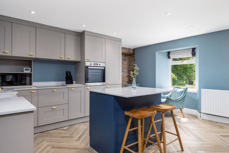 Modern kitchen with gray cabinetry, blue island, wooden bar stools, and blue accent wall
