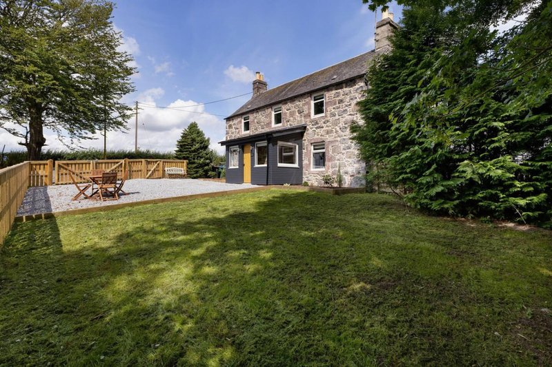 Stone cottage exterior with garden, decking, and lawn surrounded by trees