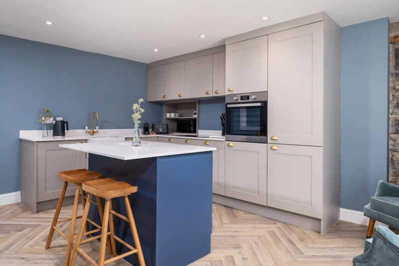 Modern kitchen with white cabinetry, blue island, wooden bar stools, and integrated appliances