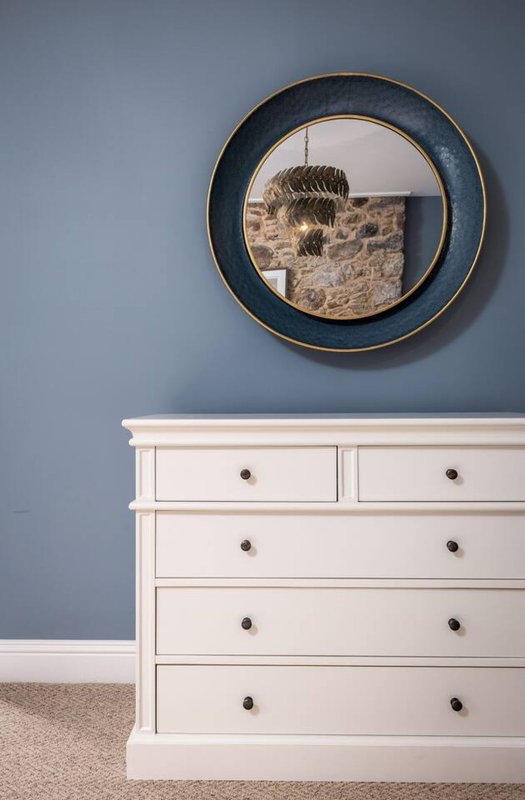 Bedroom with white chest of drawers and circular mirror on blue wall