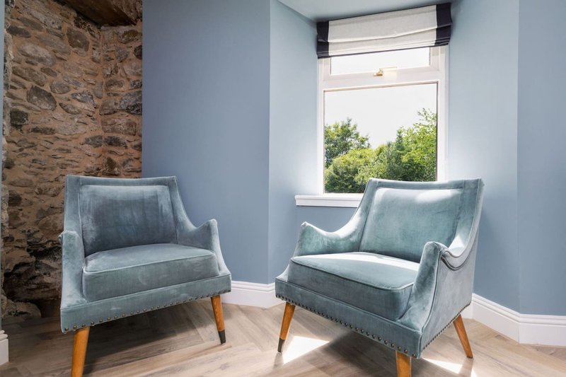 Bright room with two grey upholstered chairs, wooden legs, stone wall feature, and window view