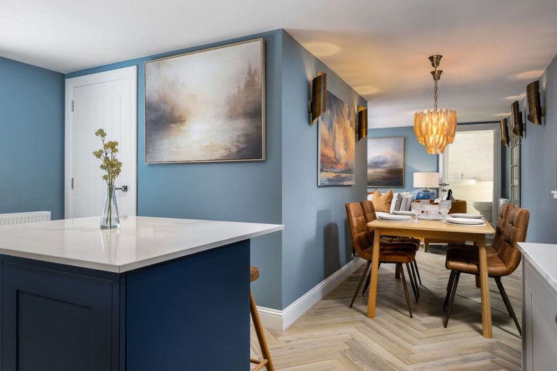 Open-plan kitchen and dining area with blue walls, island counter, wooden table and chairs, pendant light