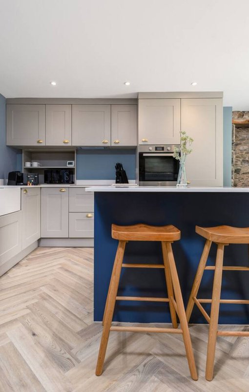 Modern kitchen with white cabinetry, blue island with wooden bar stools, and herringbone flooring