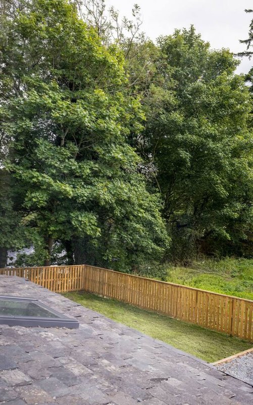 Wooden fence and paved patio area with mature trees and green lawn behind