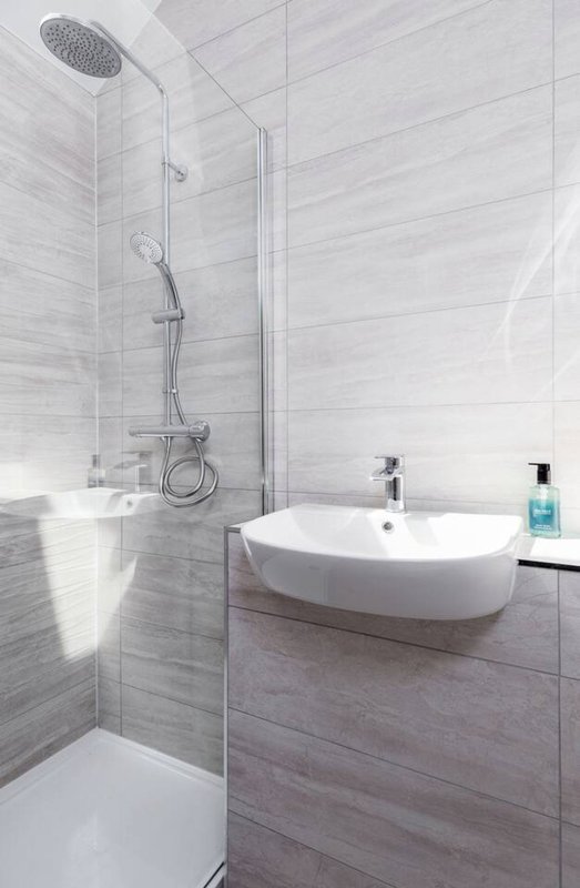 Modern bathroom with walk-in shower, curved white sink and grey tile walls