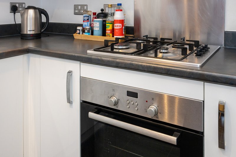 Modern kitchen with gas hob, built-in oven, stainless steel kettle and countertop condiments