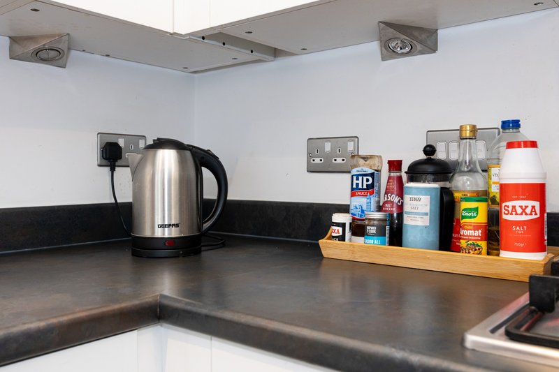 Modern kitchen counter with stainless steel kettle, electrical outlets, and shelf of condiments and household products