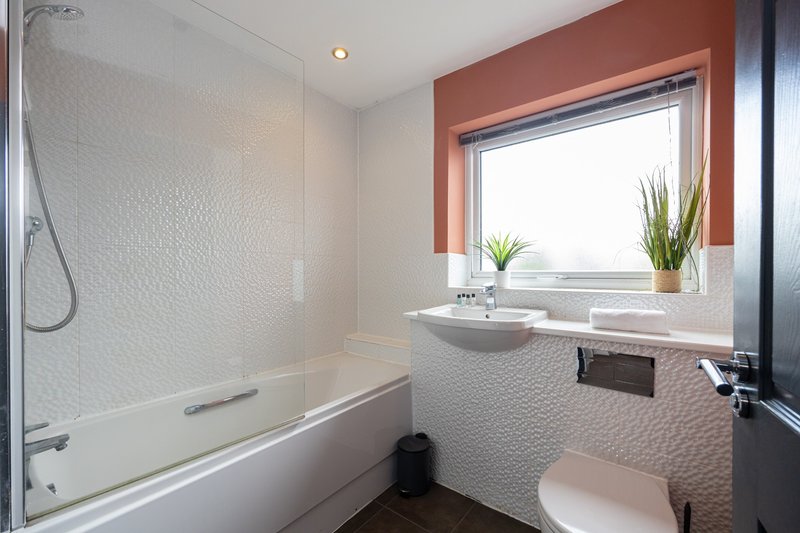 Modern bathroom with bathtub, toilet, sink, window with plants and terracotta frame