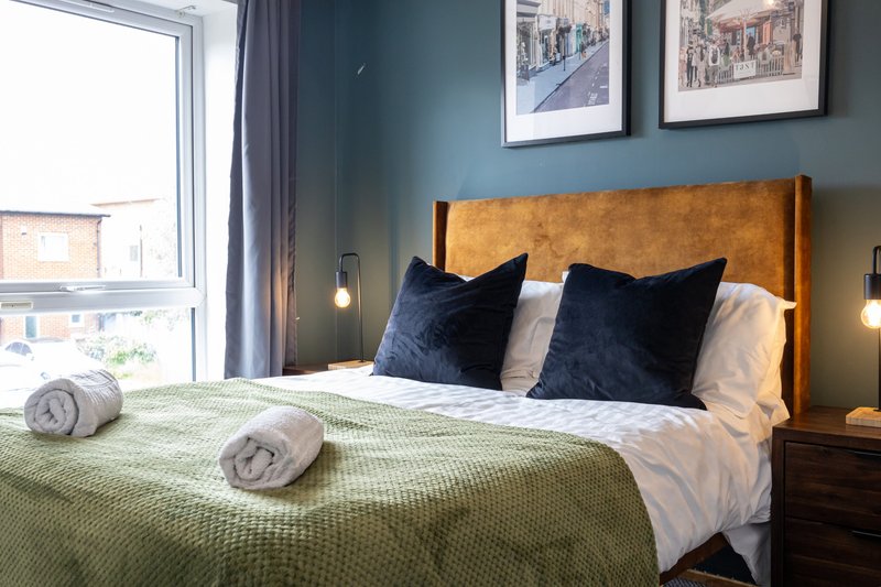 Modern bedroom with mustard headboard, green bedspread, dark pillows and framed wall art