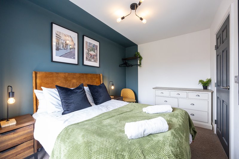 Bedroom with tan headboard, white bedding, green throw blanket, and blue accent wall